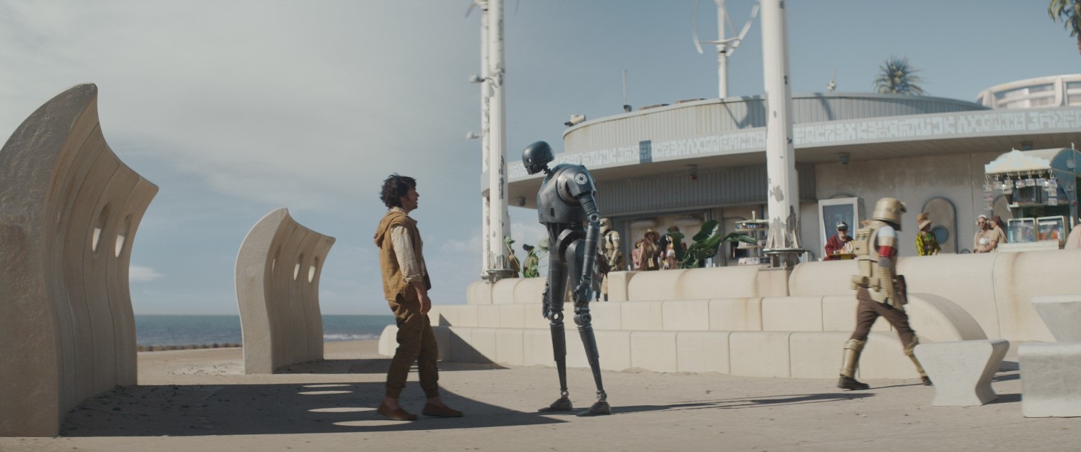 Screen capture from Star Wars Andor showing a human talking to a robot on Cleveleys beach