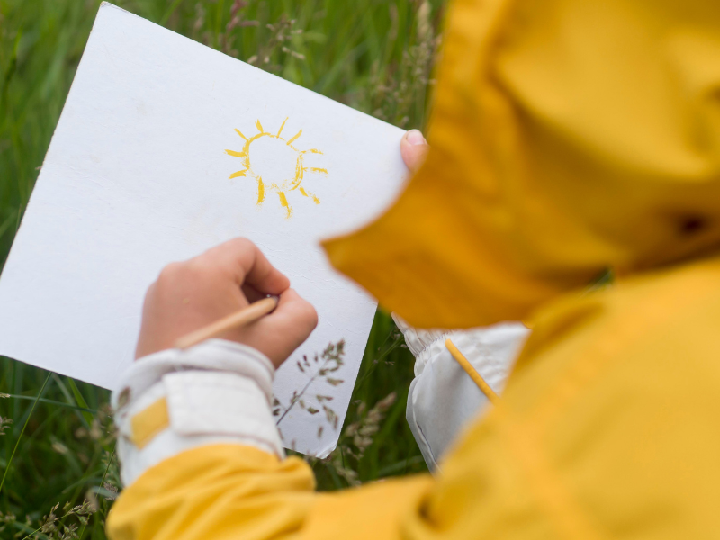 Back of child's head drawing on a piece of paper on the grass